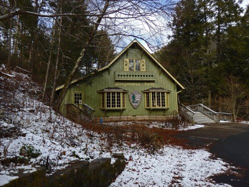 A green building with a sign reading "Dingmans Falls," surrounded by trees and a dusting of snow.