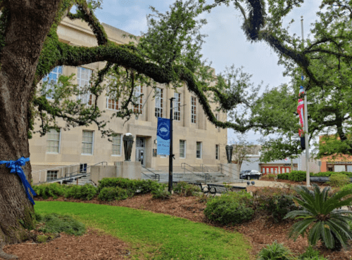 A historic building surrounded by trees and greenery, featuring flags and a blue ribbon decoration.