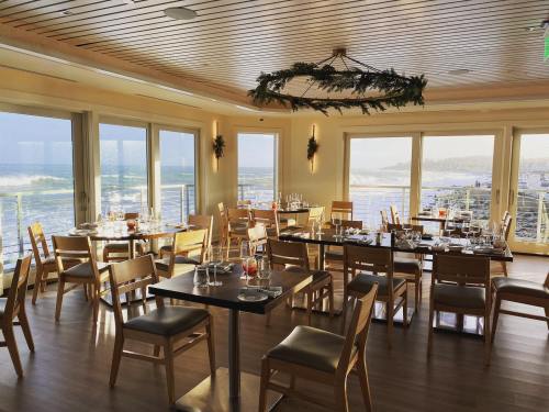 A bright restaurant with wooden tables and chairs, featuring large windows overlooking a scenic view.