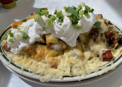 A plate of cheesy nachos topped with sour cream and green onions, featuring layers of melted cheese and diced ingredients.