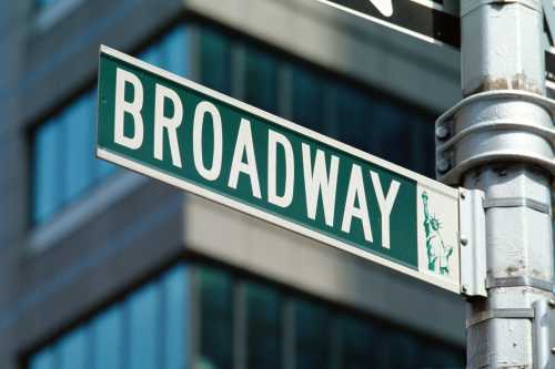 Street sign for Broadway with a blurred city background.