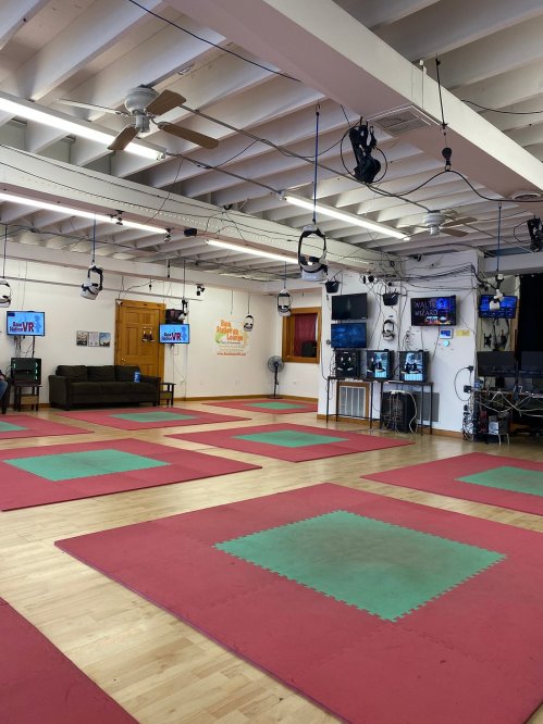 A spacious room with red and green mats, multiple screens, and VR equipment, designed for virtual reality activities.