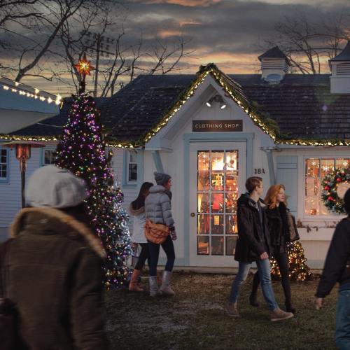 A festive clothing shop with holiday decorations, a Christmas tree, and people walking by at dusk.