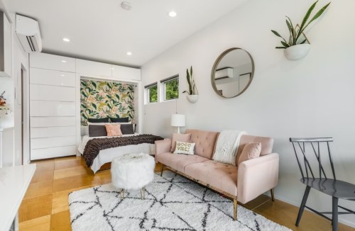 Cozy bedroom with a floral accent wall, a pink sofa, a round mirror, and stylish decor.