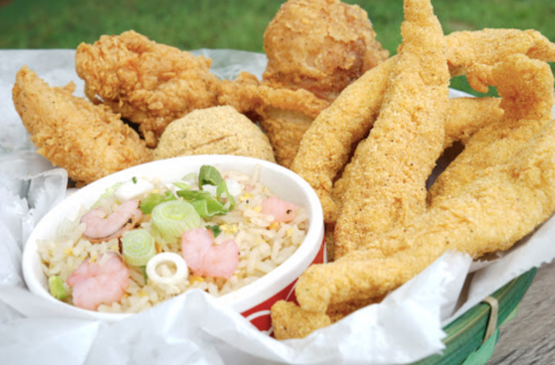 A basket of fried chicken and fish fillets, accompanied by a small bowl of fried rice with shrimp and green onions.