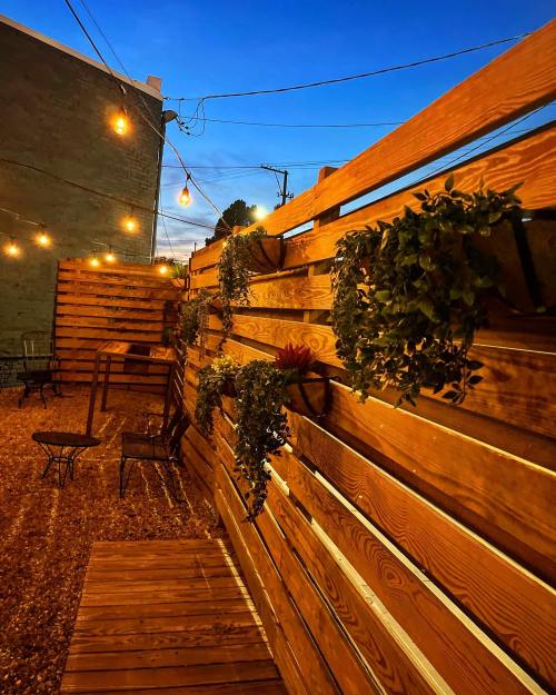A cozy outdoor space with wooden walls, hanging plants, and string lights at dusk.