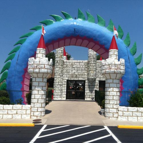 Colorful inflatable castle entrance with green and blue arch, flanked by stone towers and red flags.