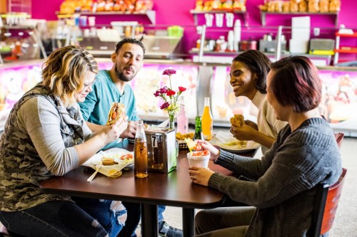 Four friends enjoy a meal together at a vibrant restaurant, sharing food and drinks with smiles and laughter.