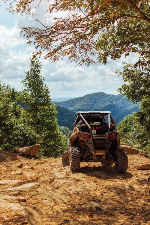 A rugged ATV parked on a rocky trail, overlooking a scenic mountain landscape under a partly cloudy sky.