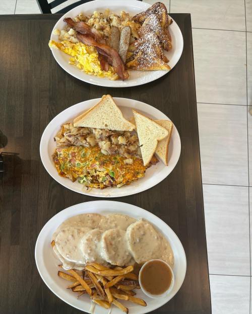 Three plates of breakfast food: scrambled eggs, bacon, sausage, French toast, an omelet, toast, biscuits with gravy, and fries.