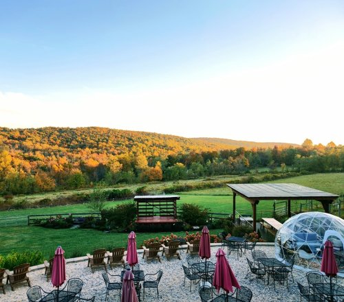 A scenic view of rolling hills with autumn foliage, featuring outdoor seating and a clear sky.