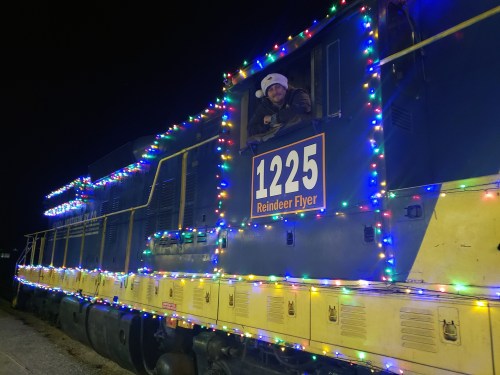 A brightly lit train decorated with colorful lights, with a person in a hat peeking out of the window at night.