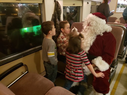 Children interacting with Santa Claus on a train, with festive decorations in the background.