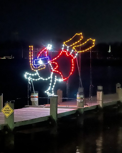 A brightly lit, festive decoration of a cartoon character on a dock at night, with a life jacket zone sign nearby.