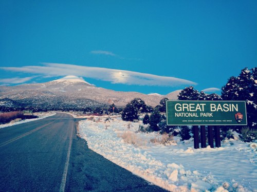Sign for Great Basin National Park with snow-covered mountains and a clear blue sky in the background.