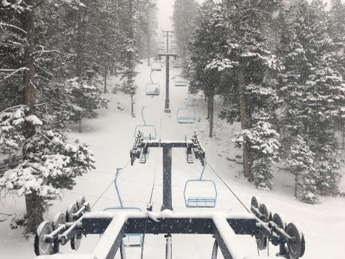 A snowy ski lift surrounded by tall trees, with heavy snowfall obscuring the view of the slope below.