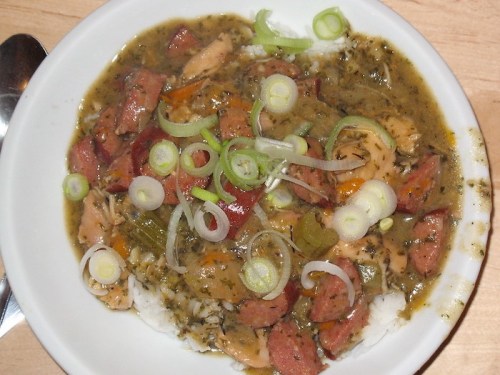 A bowl of rice topped with a savory stew featuring chicken, sausage, and green onions.