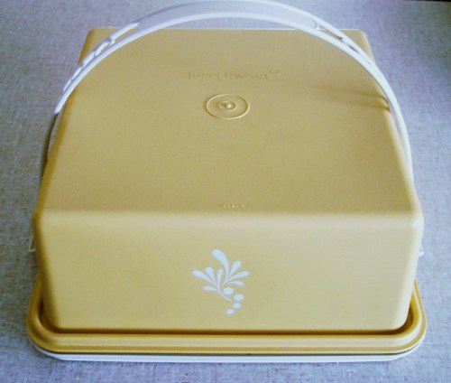 A yellow Tupperware container with a white handle and decorative design on the front, resting on a light surface.