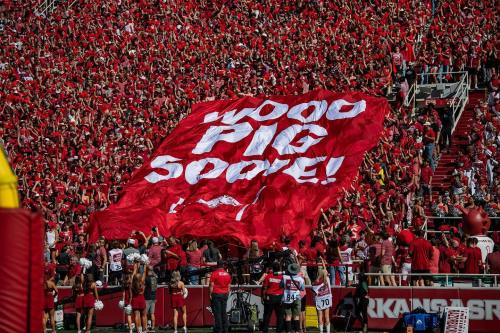 A large crowd in red clothing holds a banner reading "WOO PIG SOOEY!" at a sports event.