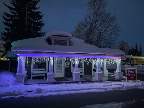 A cozy park office building covered in snow, illuminated with colorful lights at night.