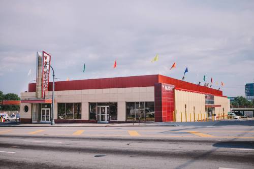 A colorful building with flags on the roof, featuring large windows and a retro-style sign, located on a busy street.
