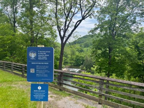 Sign marking the entrance to the West Virginia Waterfall Trail, surrounded by lush greenery and a river in the background.