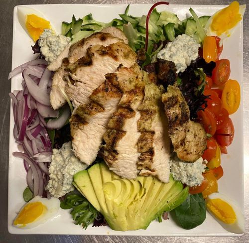 A colorful salad topped with grilled chicken, avocado, cherry tomatoes, red onion, and blue cheese on a bed of greens.