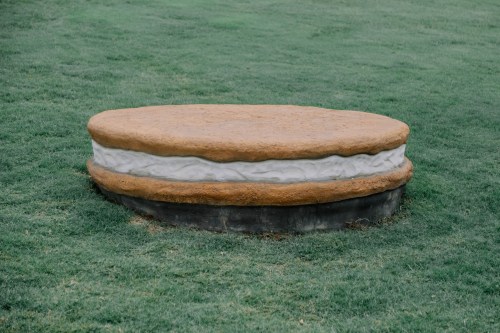 A large, round sculpture resembling a sandwich cookie sits on green grass.