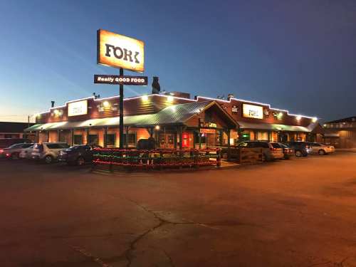 A restaurant named "Fork" with bright signage, festive lights, and parked cars in the evening.