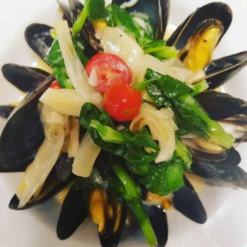 A plate of mussels topped with cherry tomatoes, onions, and greens, arranged beautifully.