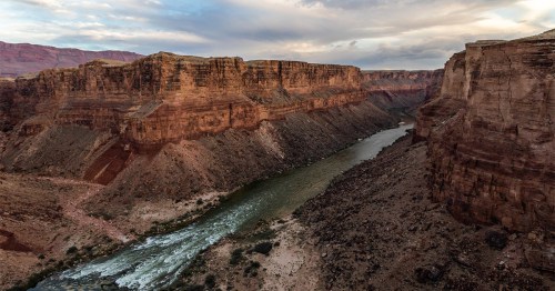 A scenic view of a winding river surrounded by towering red rock cliffs under a cloudy sky.