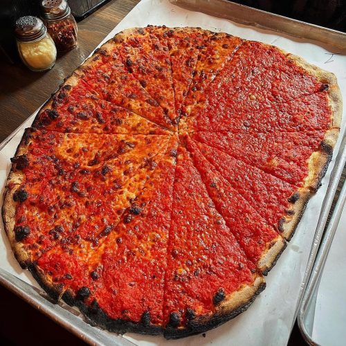 A large, rectangular pizza with a crispy crust, topped with vibrant red sauce and evenly sliced into triangular pieces.