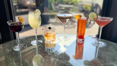 A variety of colorful cocktails on a table, including a martini, a highball, and a fruity drink, in a bright setting.