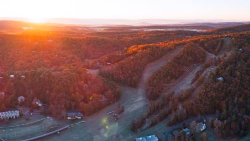 Aerial view of a mountainous landscape at sunset, showcasing vibrant autumn foliage and ski slopes.