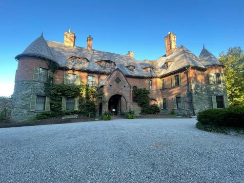 A large, historic mansion with a mix of brick and stone, featuring a grand entrance and surrounded by greenery.