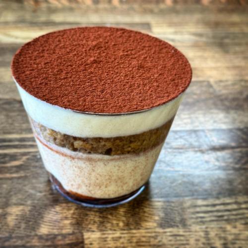A glass dessert layered with creamy mascarpone, coffee-soaked cake, and topped with cocoa powder.