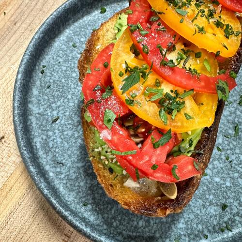 A slice of toasted bread topped with colorful tomato slices and fresh herbs on a gray plate.