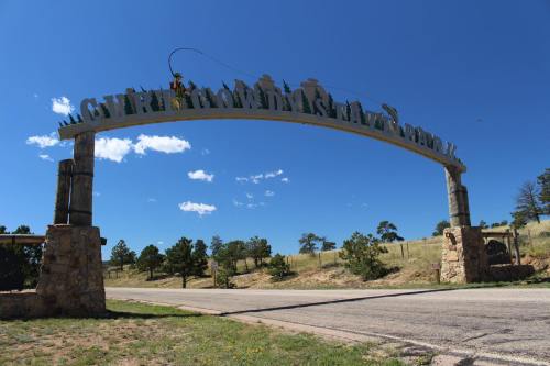 Archway sign for Curly Creek State Park against a clear blue sky, with trees and a road in the background.