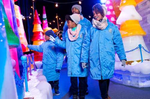 A family in blue jackets explores a colorful ice exhibit, surrounded by vibrant ice sculptures and festive lights.