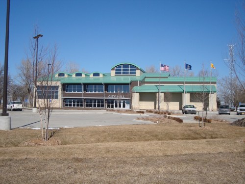 Modern city hall building with a green roof, flags, and a clear blue sky in the background.