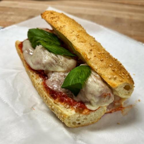 A sesame seed hoagie filled with meatballs, marinara sauce, melted cheese, and fresh basil leaves.