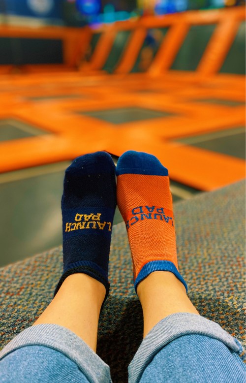 A pair of feet wearing mismatched socks, one blue and one orange, resting on a colorful trampoline surface.