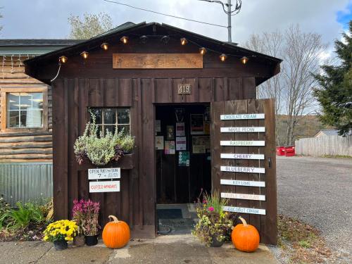 A rustic wooden shop entrance with pumpkins, flowers, and a sign listing various ice cream flavors.