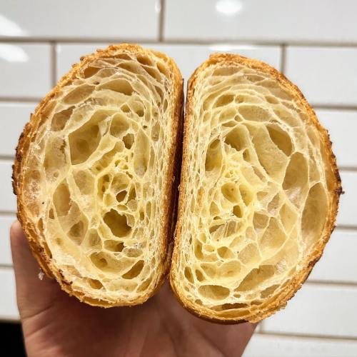 A hand holding a freshly cut croissant, showcasing its flaky, airy interior and golden-brown crust.