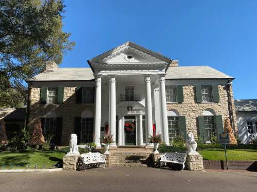 A large, elegant stone mansion with white columns, green shutters, and festive decorations in front.