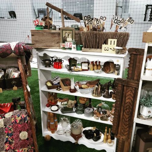 A vintage display shelf filled with various antiques, tools, and decorative items, set in a market environment.