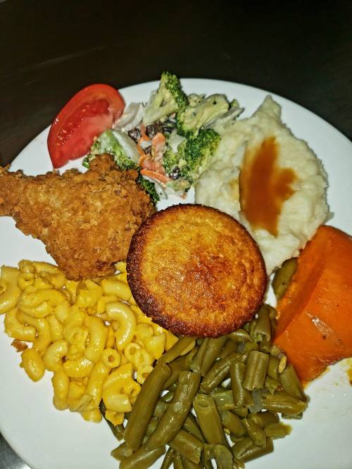 A plate of fried chicken, macaroni and cheese, green beans, broccoli salad, mashed potatoes with gravy, cornbread, and sweet potato.