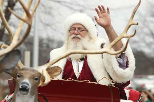 Santa Claus waves from a festive sleigh, with reindeer antlers in the foreground and a wintery background.