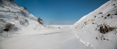 A snowy landscape with a narrow path between snow-covered hills under a clear blue sky.