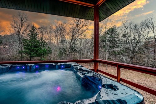 A hot tub on a deck with a scenic view of trees and a colorful sunset sky in the background.